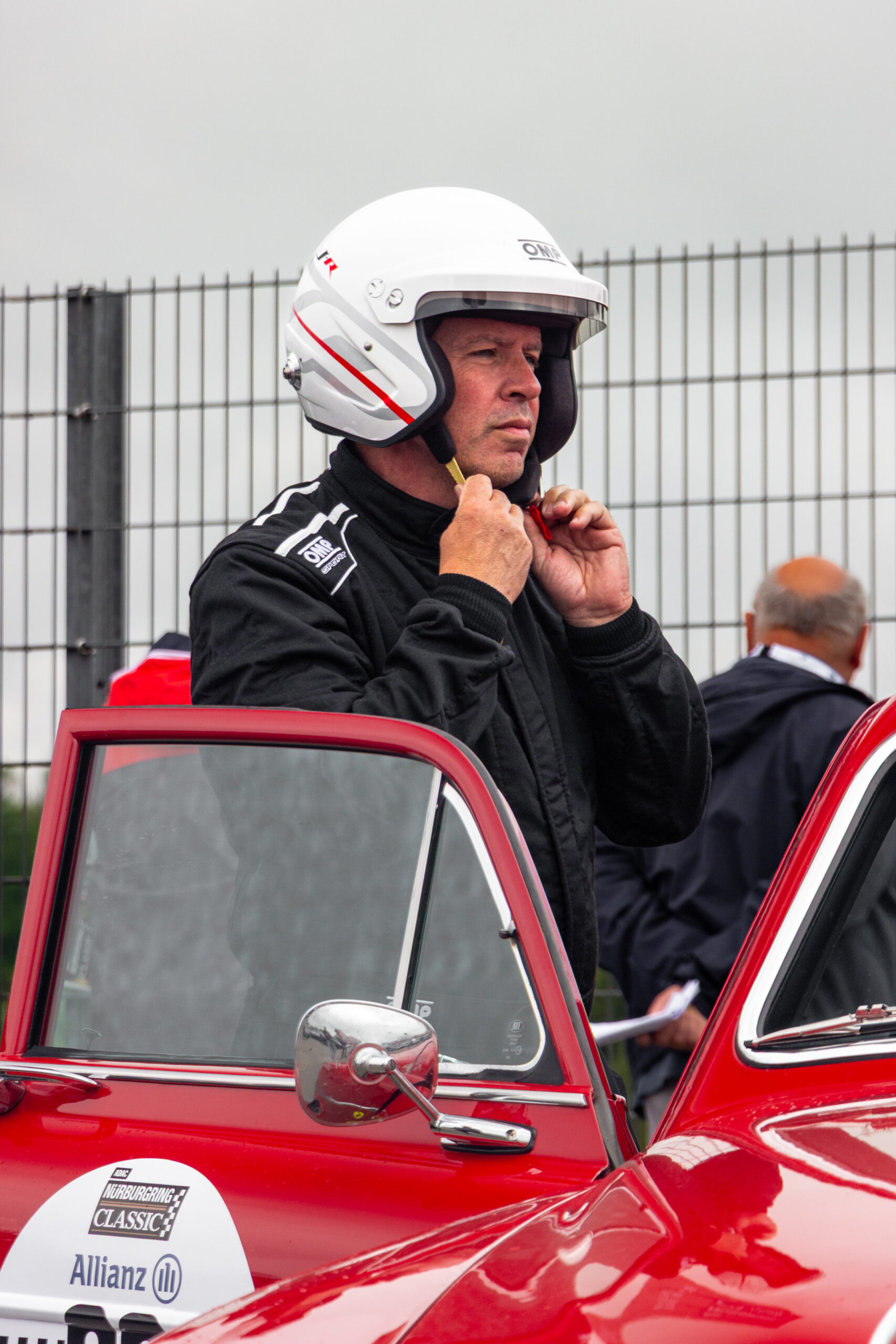 Ein Rennfahrer im Rennoverall zieht seinen Helm für die GLP Track Masters am Nürburgring auf.
